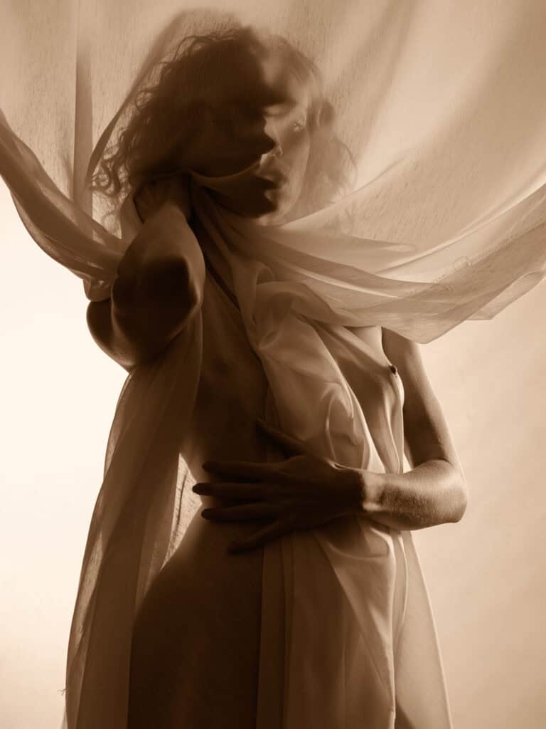 Photo artistique d'une femme avec tissu fluide et lumière douce, style créatif et esthétique.