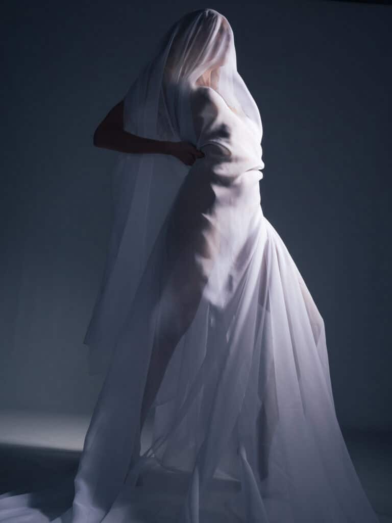 Corps féminin sous tissu blanc, jeu de lumière créant une silhouette artistique moderne.
