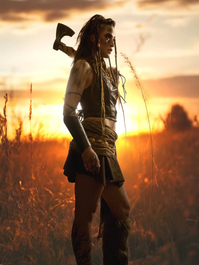 Femme guerrière avec hache dans un champ au coucher du soleil, style fantasy et aventure.