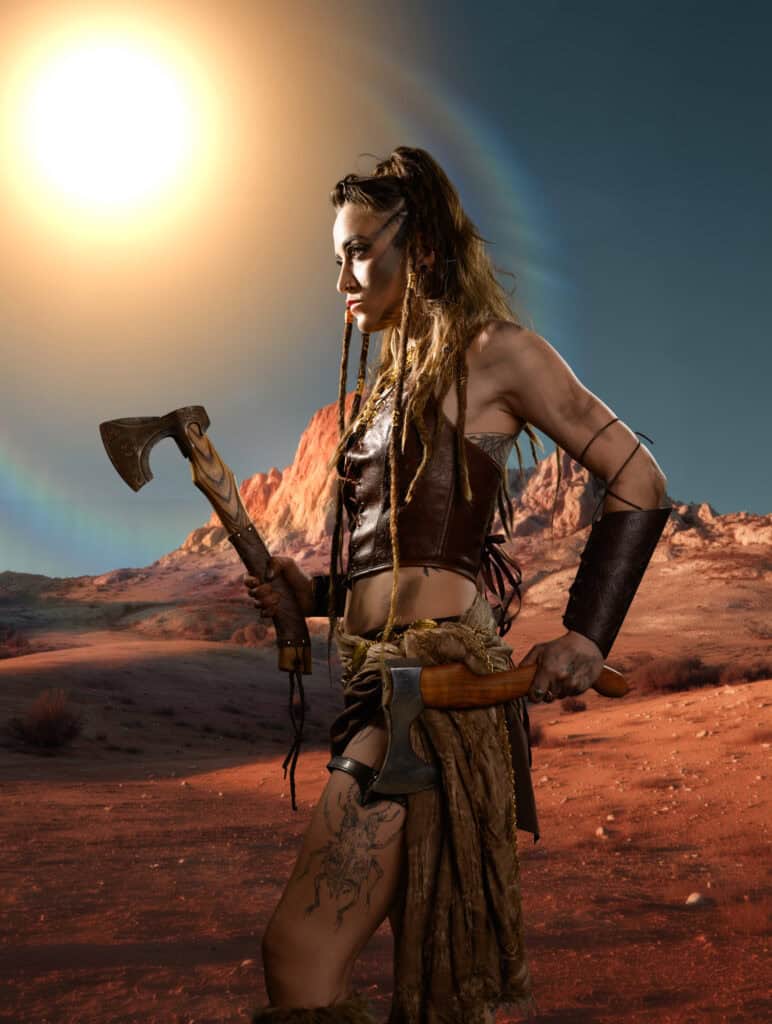 Femme en costume de guerrière avec hache dans un paysage désertique aride.
