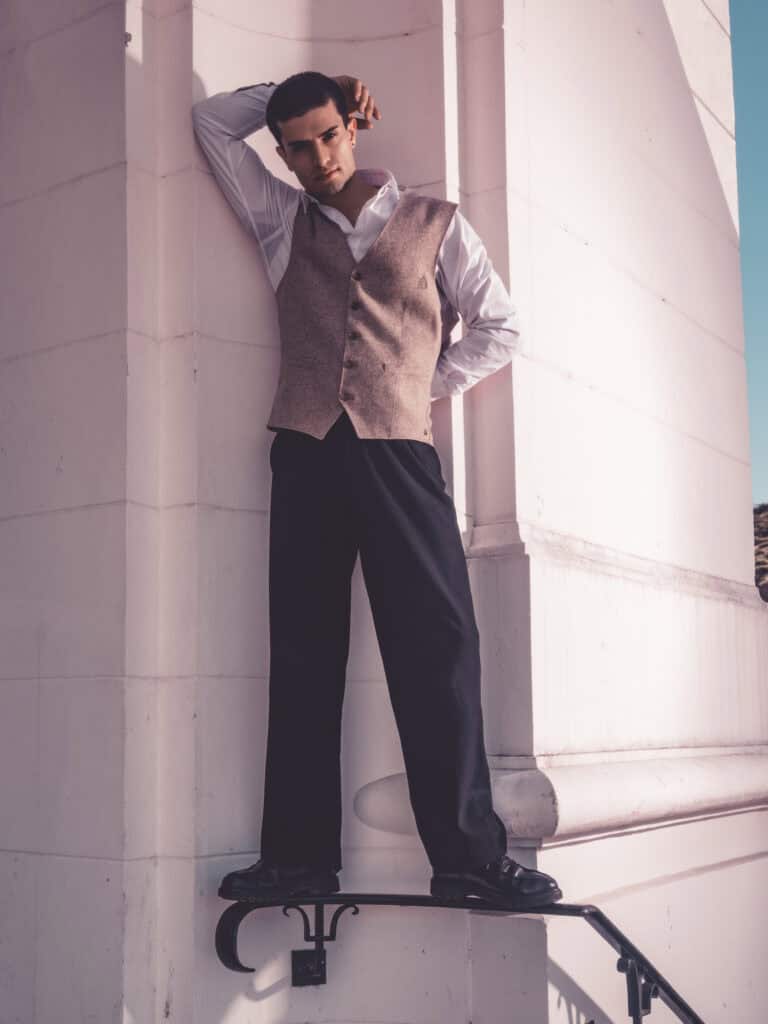 Homme en tenue chic posant contre un mur en pierre blanche.