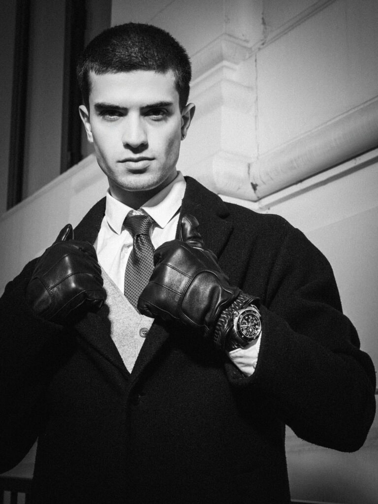 Homme en costume noir avec gants en cuir, look sophistiqué et sérieux.