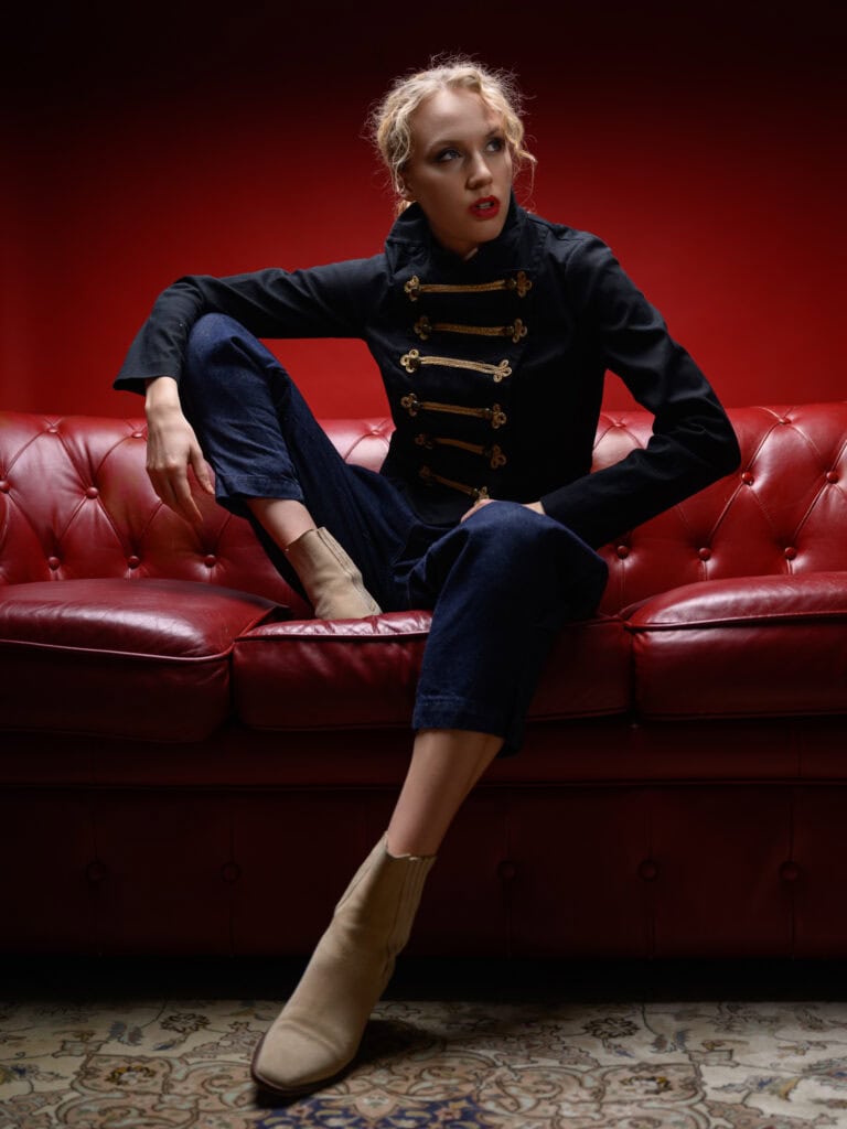 Femme en veste militaire élégante sur un canapé rouge, style mode sophistiqué.