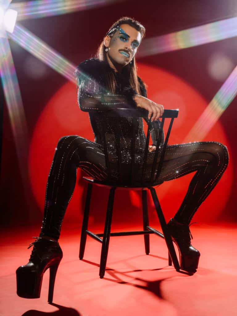 Photo artistique d'une performeuse en costume brillant et maquillage expressif, posant sur une chais.