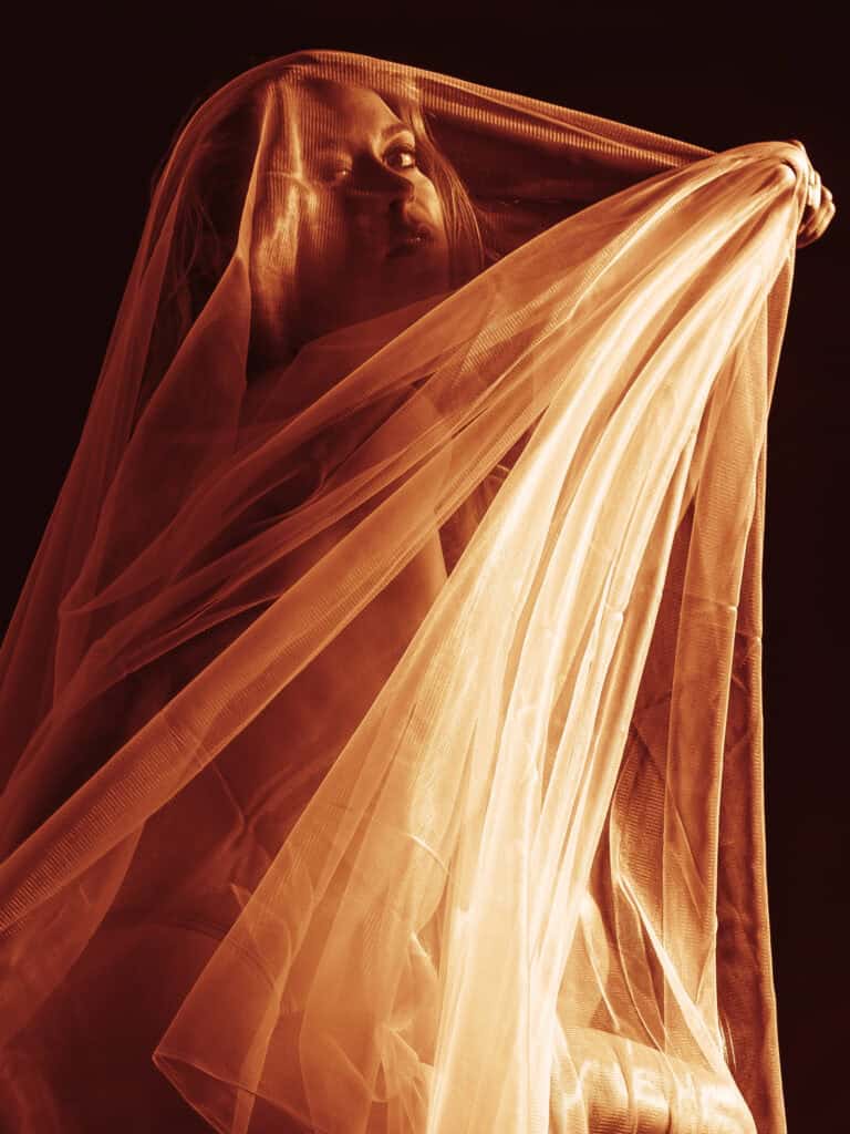 Tissu translucide enveloppant une femme, jeu de lumière et d'ombres.