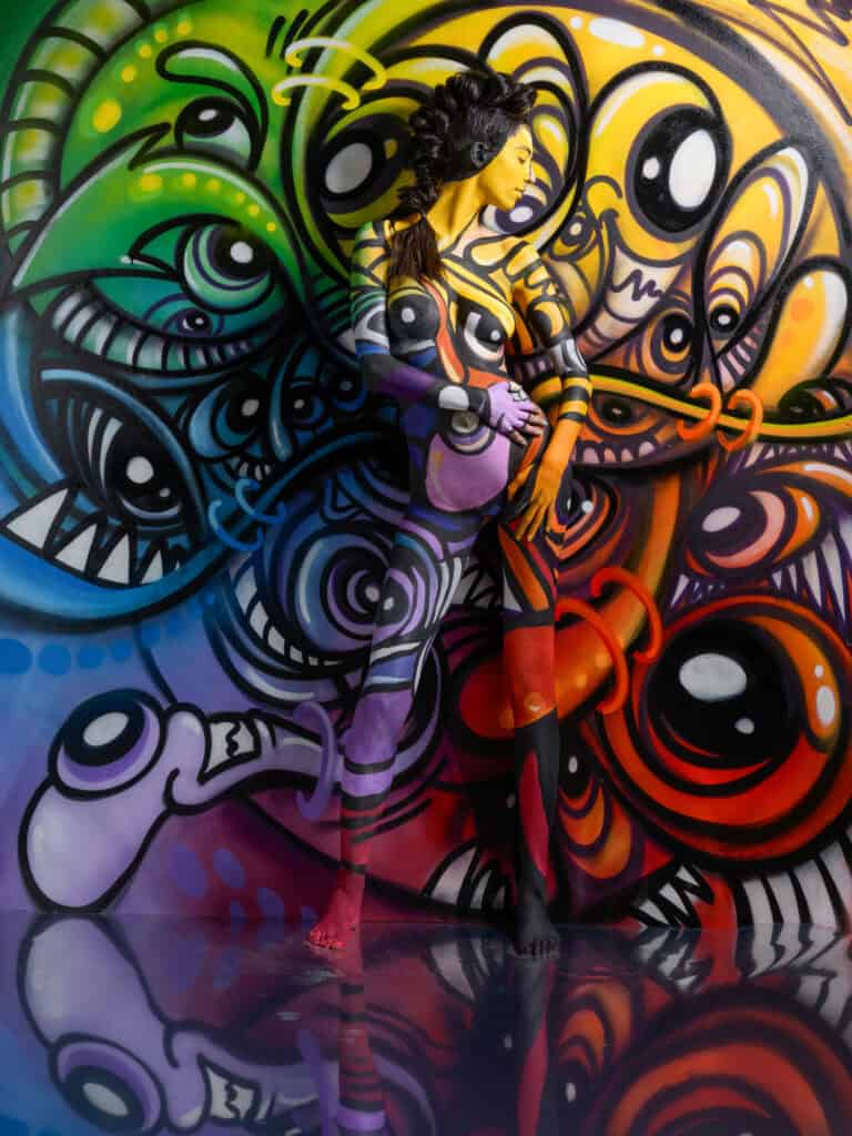Femme en body peint avec un mural abstrait coloré au studio Coloria.