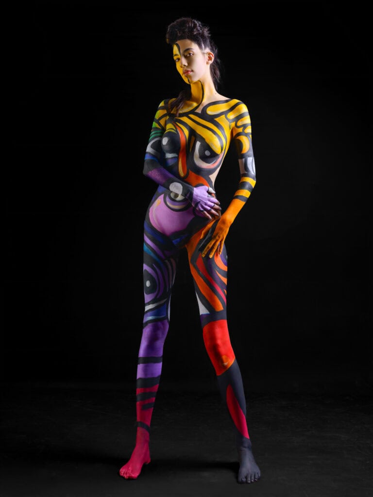 Modèle peint à la main avec motifs colorés sur corps entier, pose artistique en studio.