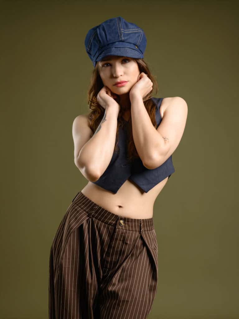 Modèle féminine portant un chapeau en denim et un haut sans manches dans un studio professionnel.
