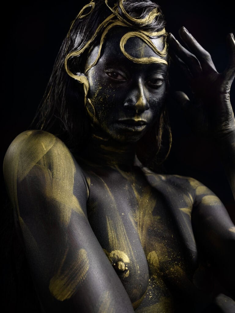 Femme peinte en noir et or avec coiffure artistique et regard intense.