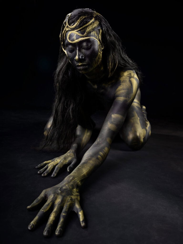 Corps peint en noir et or avec maquillage artistique sur fond noir.