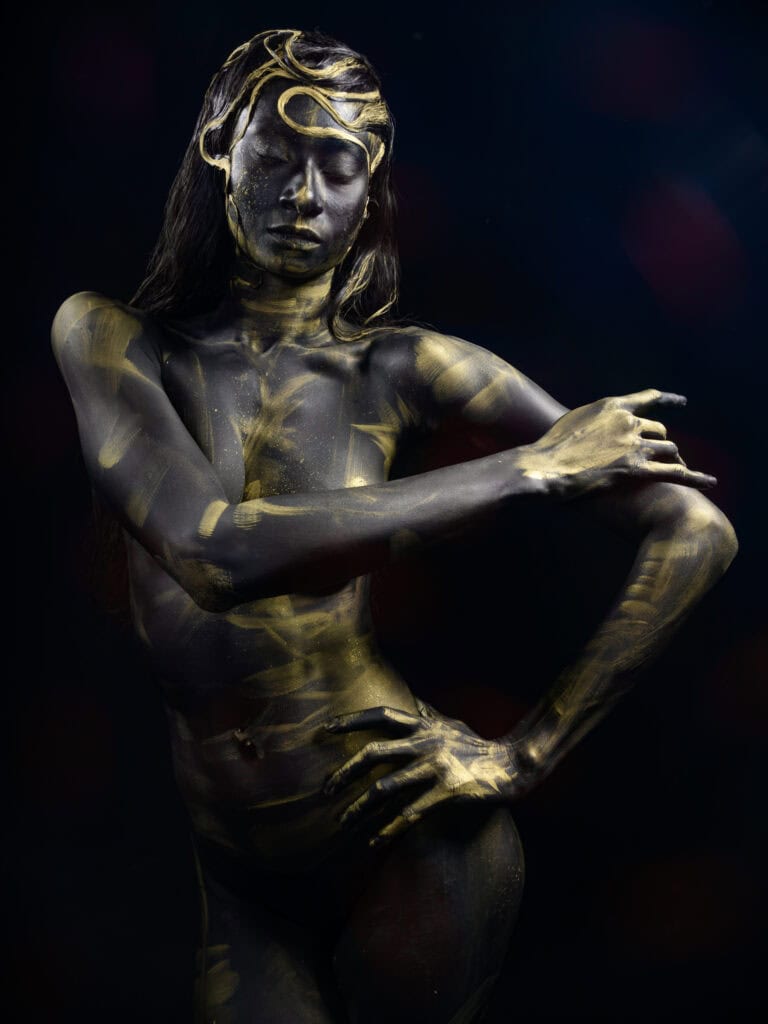 Modèle artistique avec peinture corporelle dorée, pose expressive et lumière dramatique.