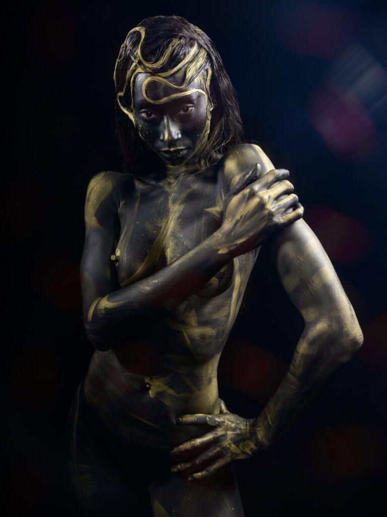 Femme peinte en or avec pose artistique et regard intense.