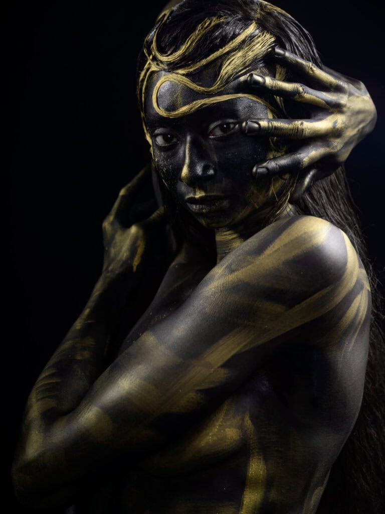 Modèle avec maquillage et body painting doré sur fond noir.