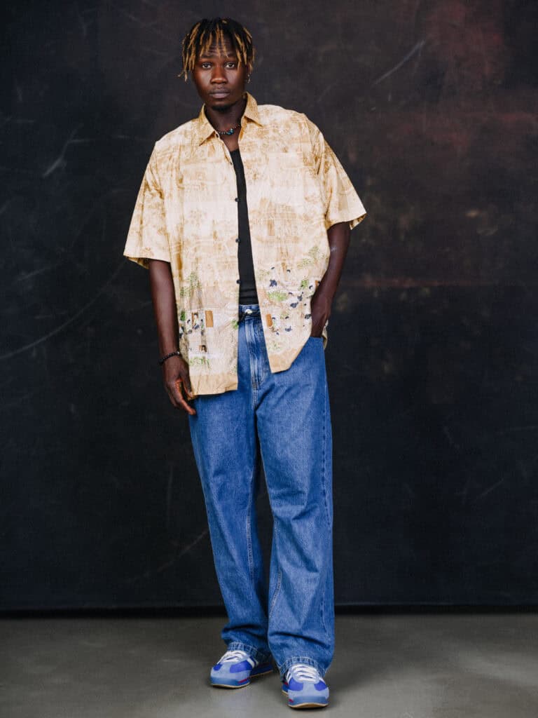 Jeune homme portant un look streetwear avec chemise beige et jeans amples, style urbain moderne.