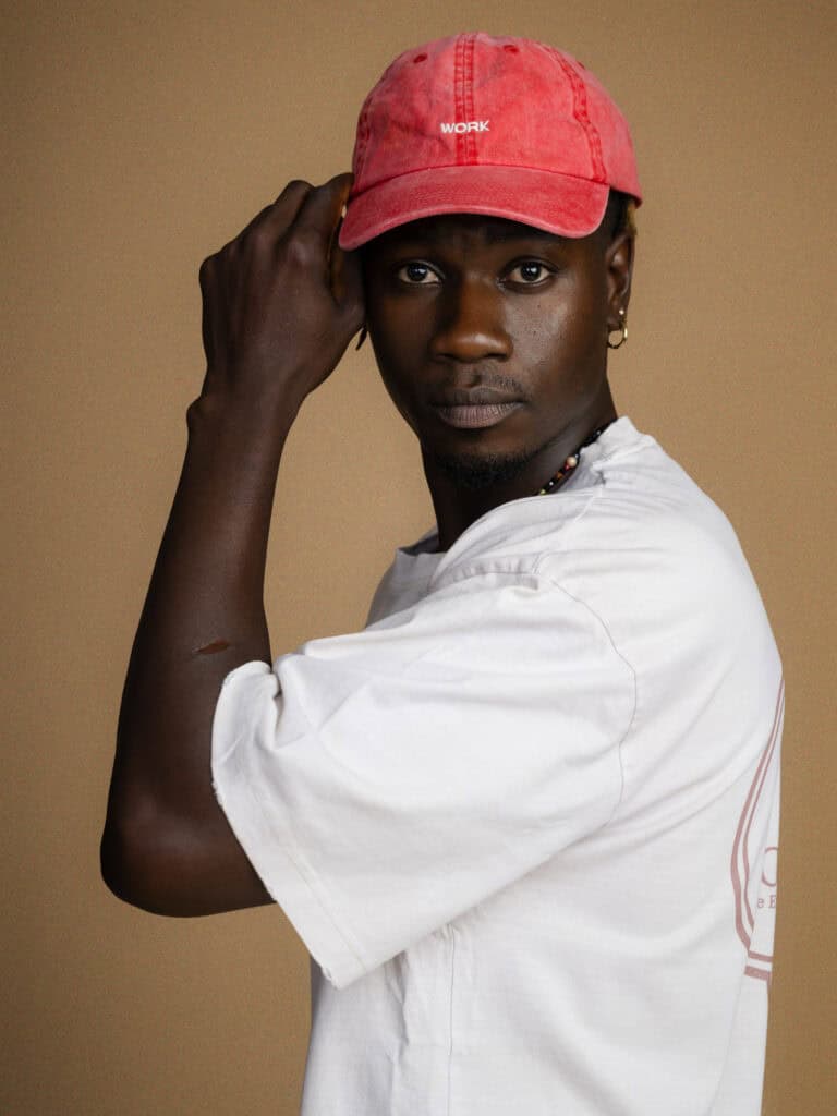 Portrait d'un jeune homme avec casquette rouge et t-shirt blanc, regard intense.