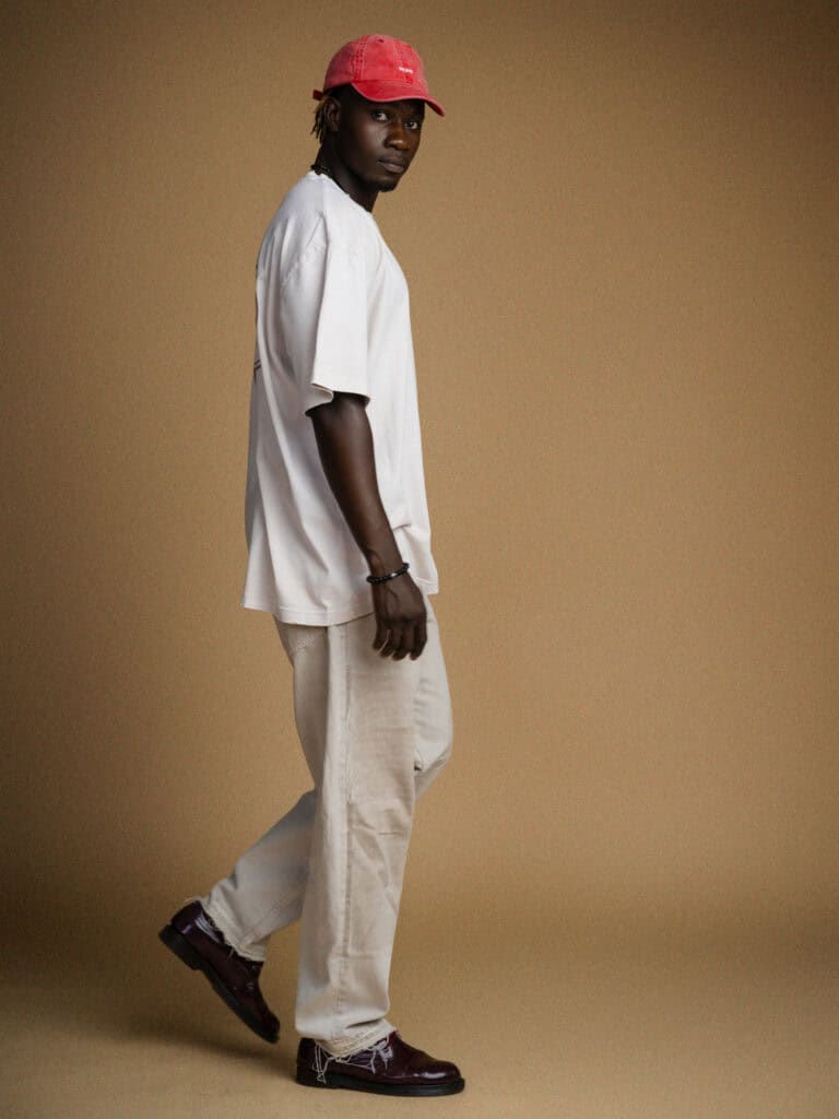 Homme portant un t-shirt blanc, pantalon beige, casquette rouge, chaussures noires.
