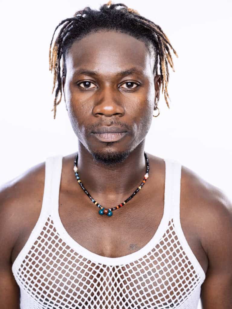 Portrait d'un homme avec dreadlocks, portant un débardeur en filet blanc et un collier coloré, regar.