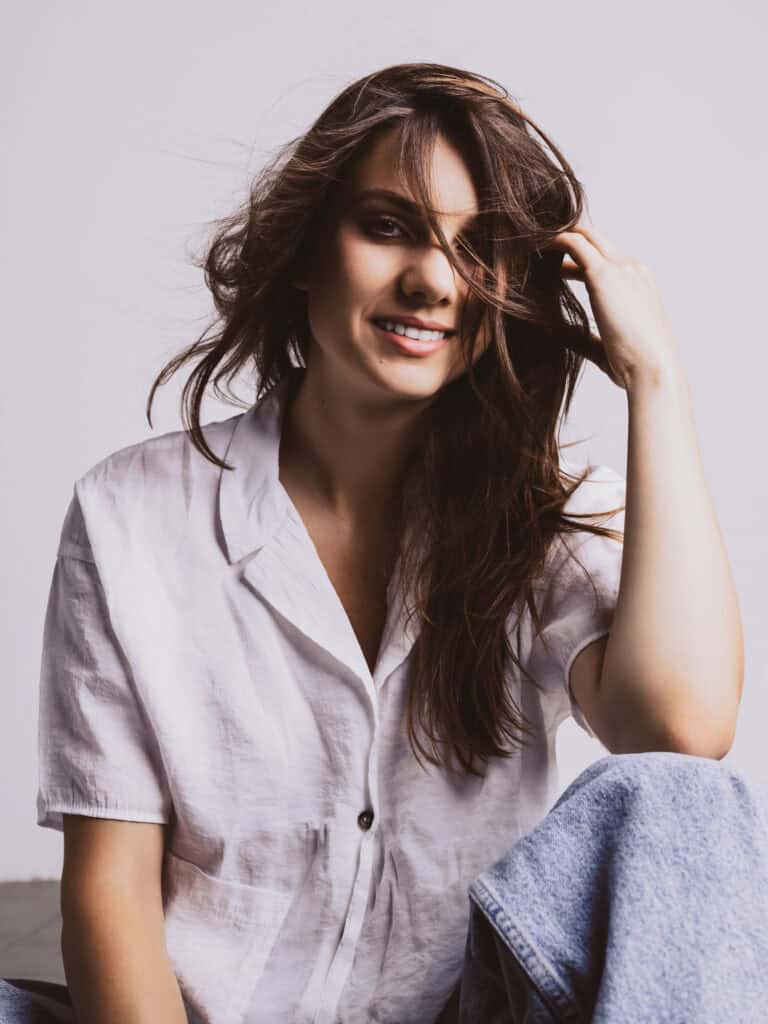 Femme souriante avec cheveux bruns et vêtements décontractés en studio.