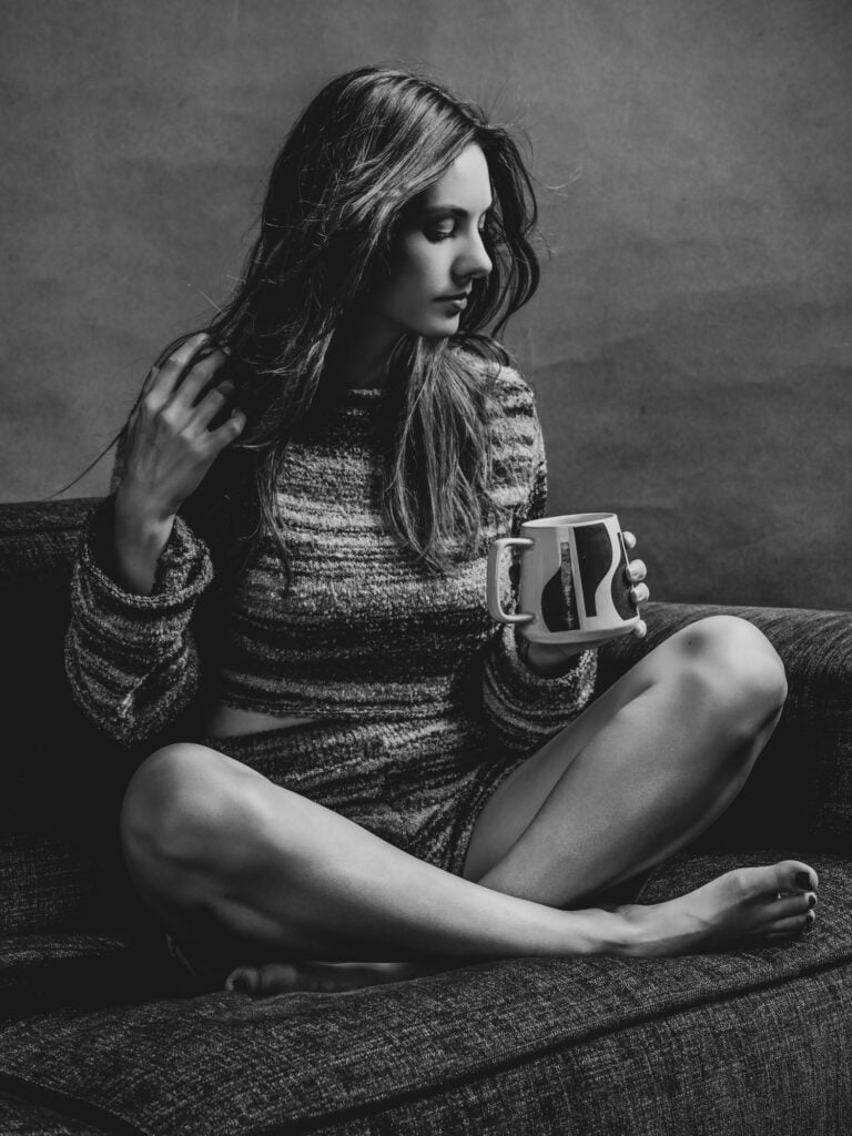 Jeune femme assise avec tasse dans un studio photo noir et blanc.