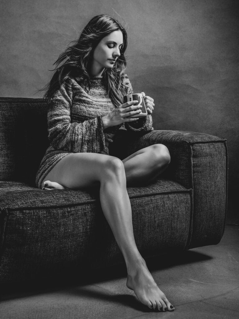 Femme assise sur un canapé, tenant une tasse, en noir et blanc.