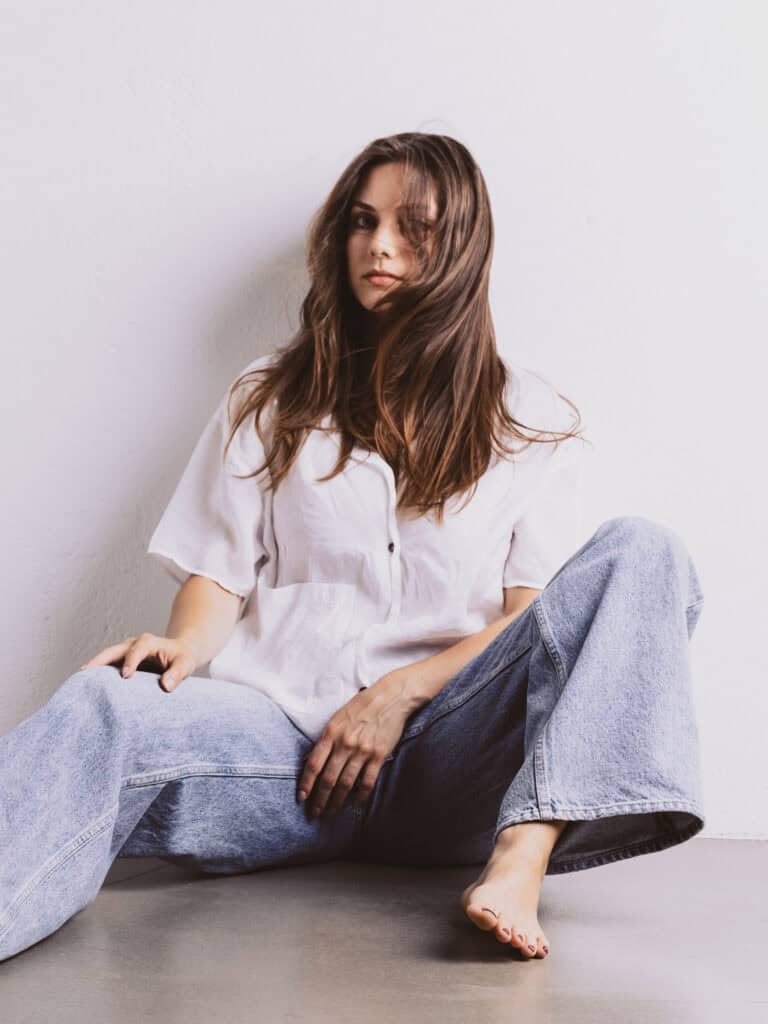 Femme assise en studio avec vêtements décontractés et cheveux longs.