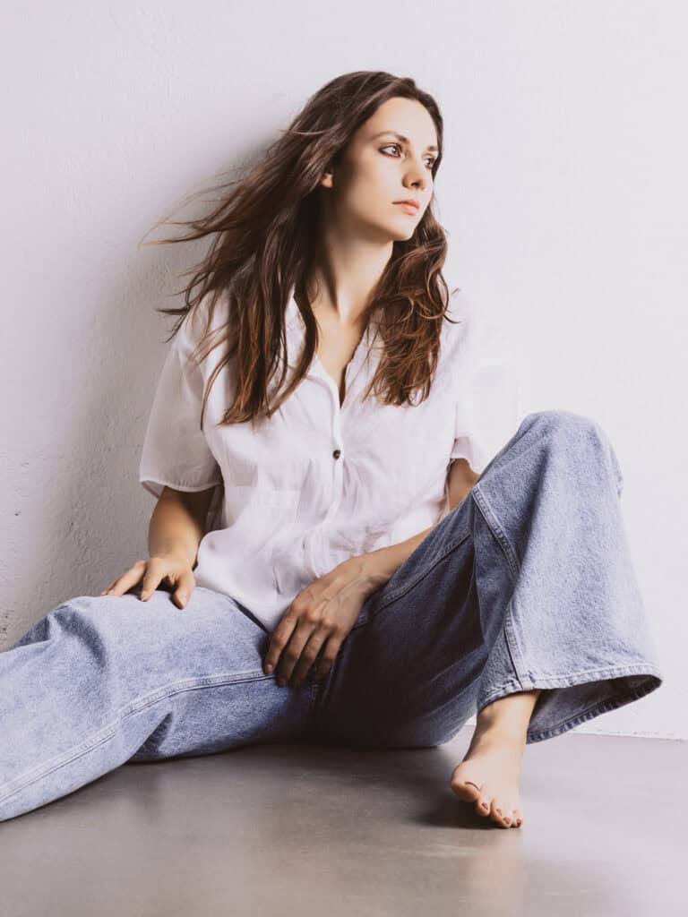 Femme en tenue décontractée assise contre un mur blanc.