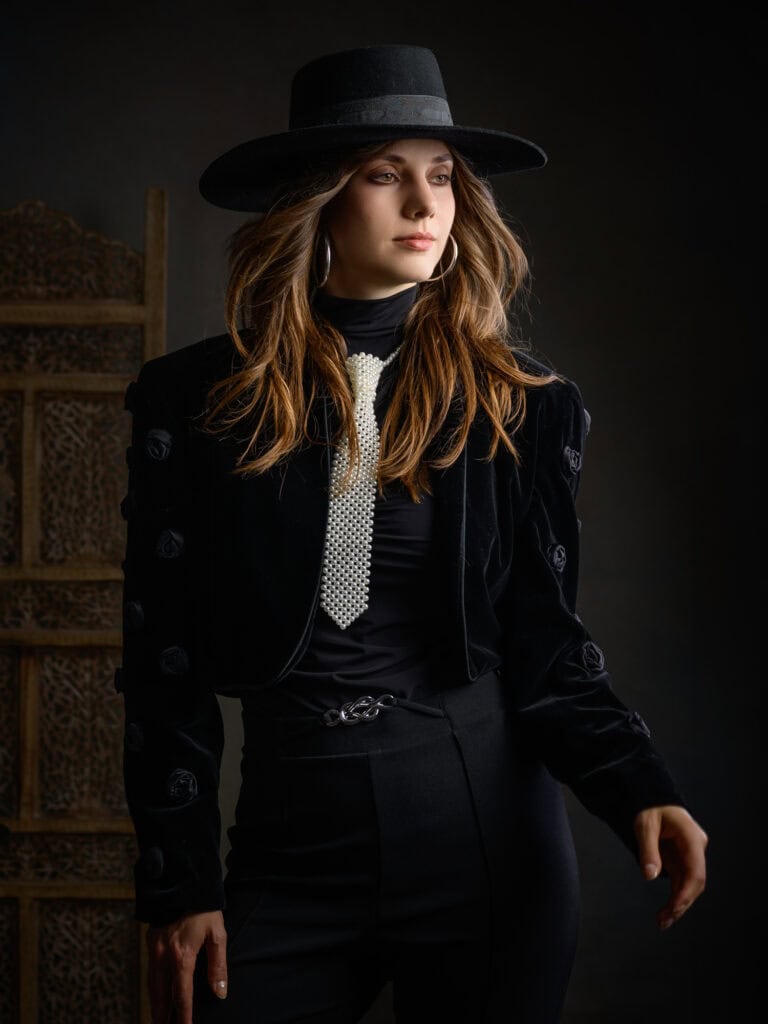 Femme élégante portant un chapeau noir et une tenue noire sophistiquée.
