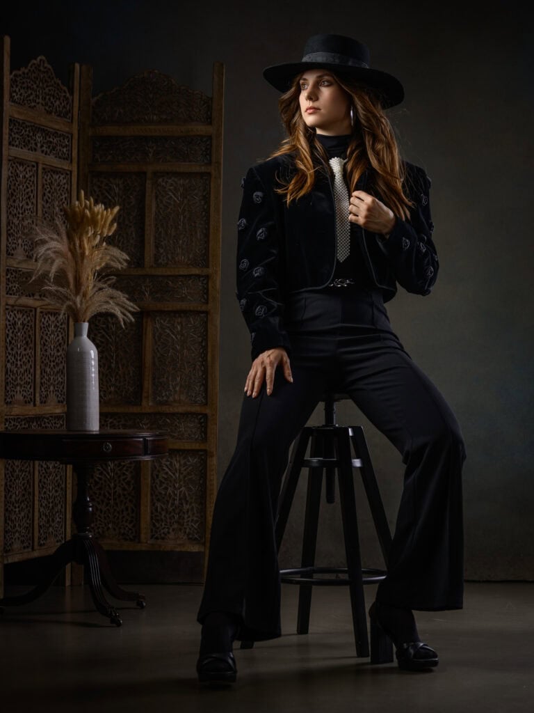 Portrait d'une femme en tenue noire avec chapeau dans un studio professionnel.