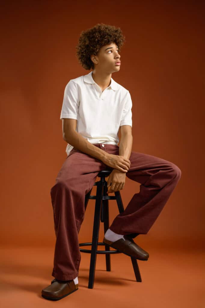 Jeune homme assise sur une chaise dans un studio avec fond marron.