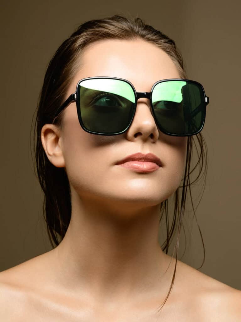 Femme portant de grandes lunettes de soleil noires et vertes, regardant vers l'avant.