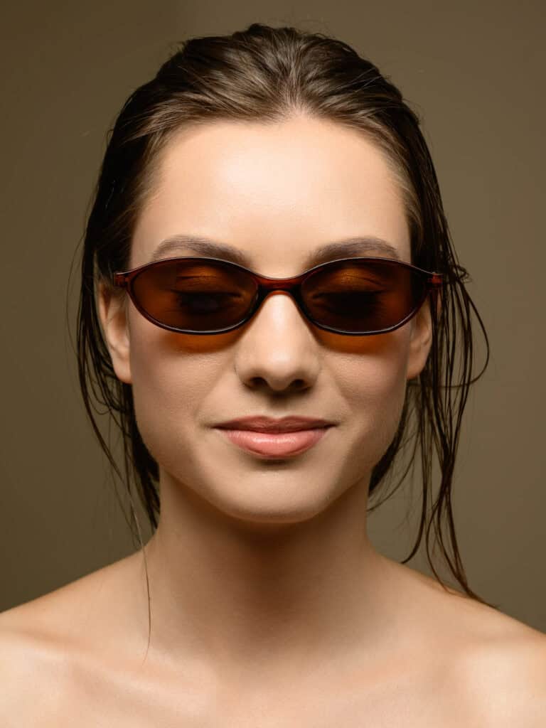 Femme élégante portant des lunettes de soleil foncées, souriant légèrement.