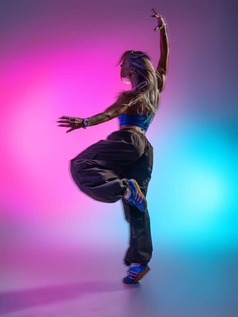 Danseuse en pose dynamique avec éclairage coloré vibrant.