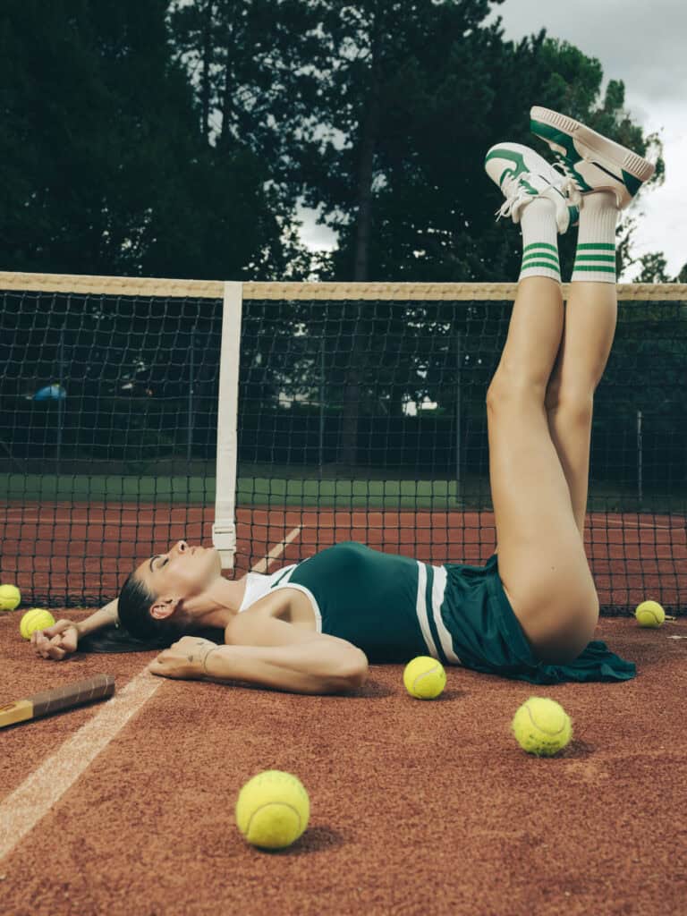 Femme allongée sur un court de tennis avec des balles de tennis autour.