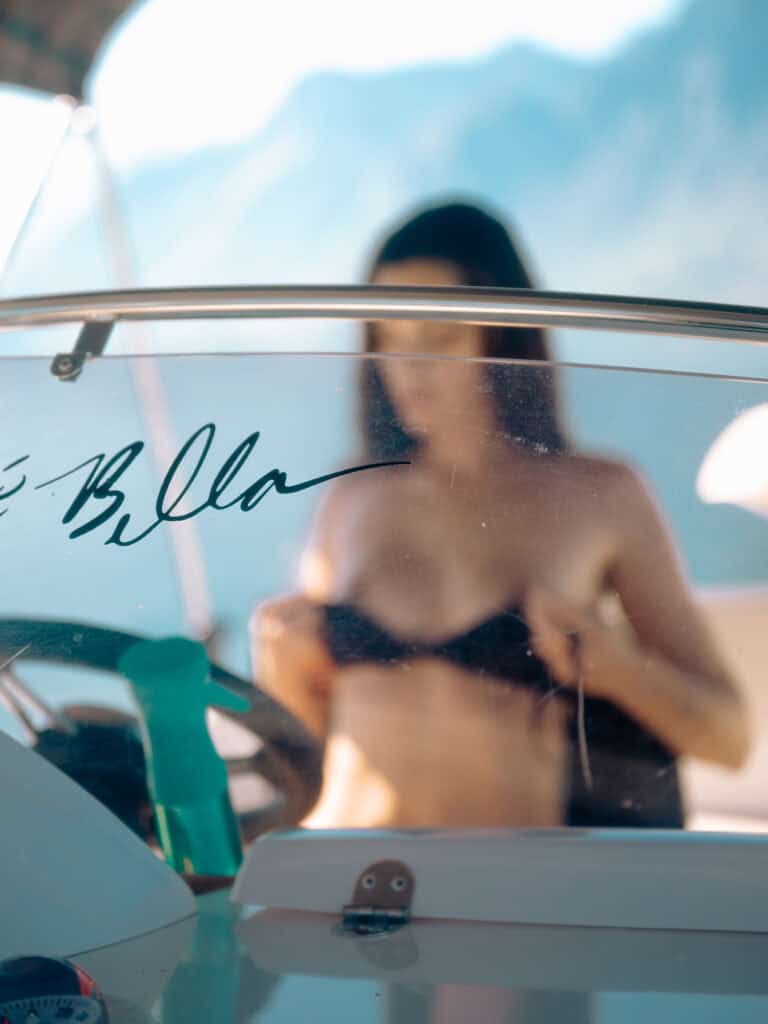 Modèle en maillot de bain sur un bateau avec vue sur la mer et montagnes en arrière-plan.