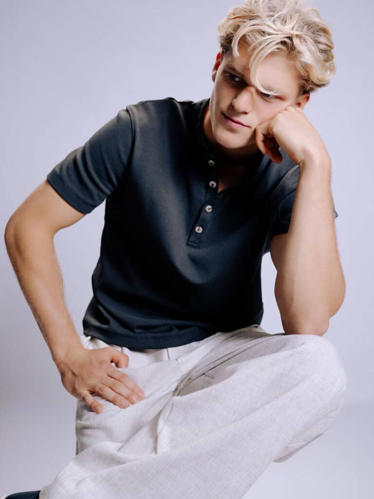 Jeune homme pensif avec cheveux blonds et chemise noire.