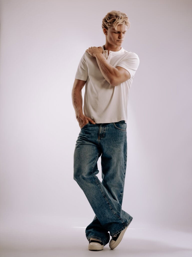 Jeune homme en t-shirt blanc et jeans, pose décontractée en studio.