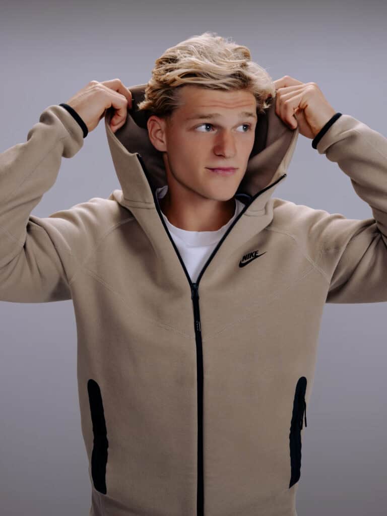 Jeune homme portant une veste beige Nike avec capuche, regardant à gauche.