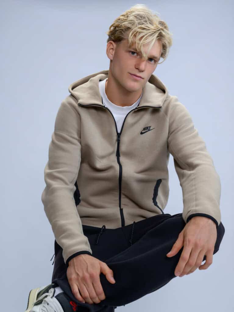 Jeune homme avec sweat Nike beige, pose décontractée, fond gris clair.